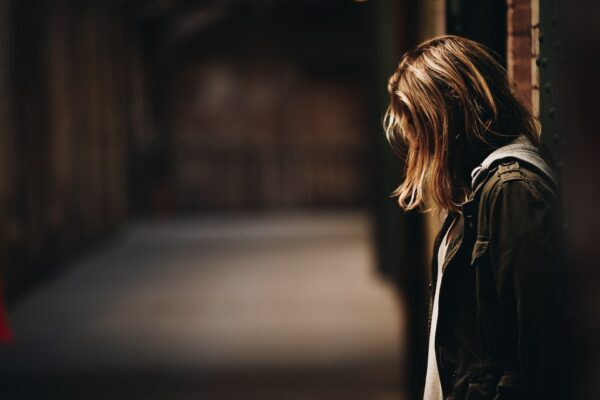 profile of scared young girl leaning against a wall, hair covering her face to promote safeguarding course